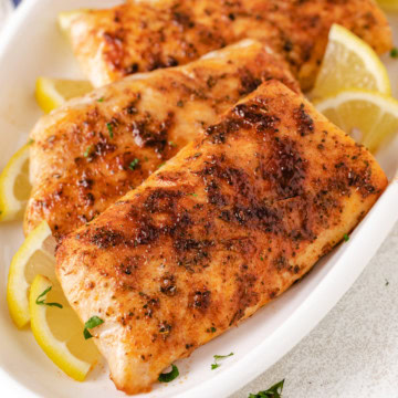 Air fryer mahi mahi fillets with lemon slices on a white platter.