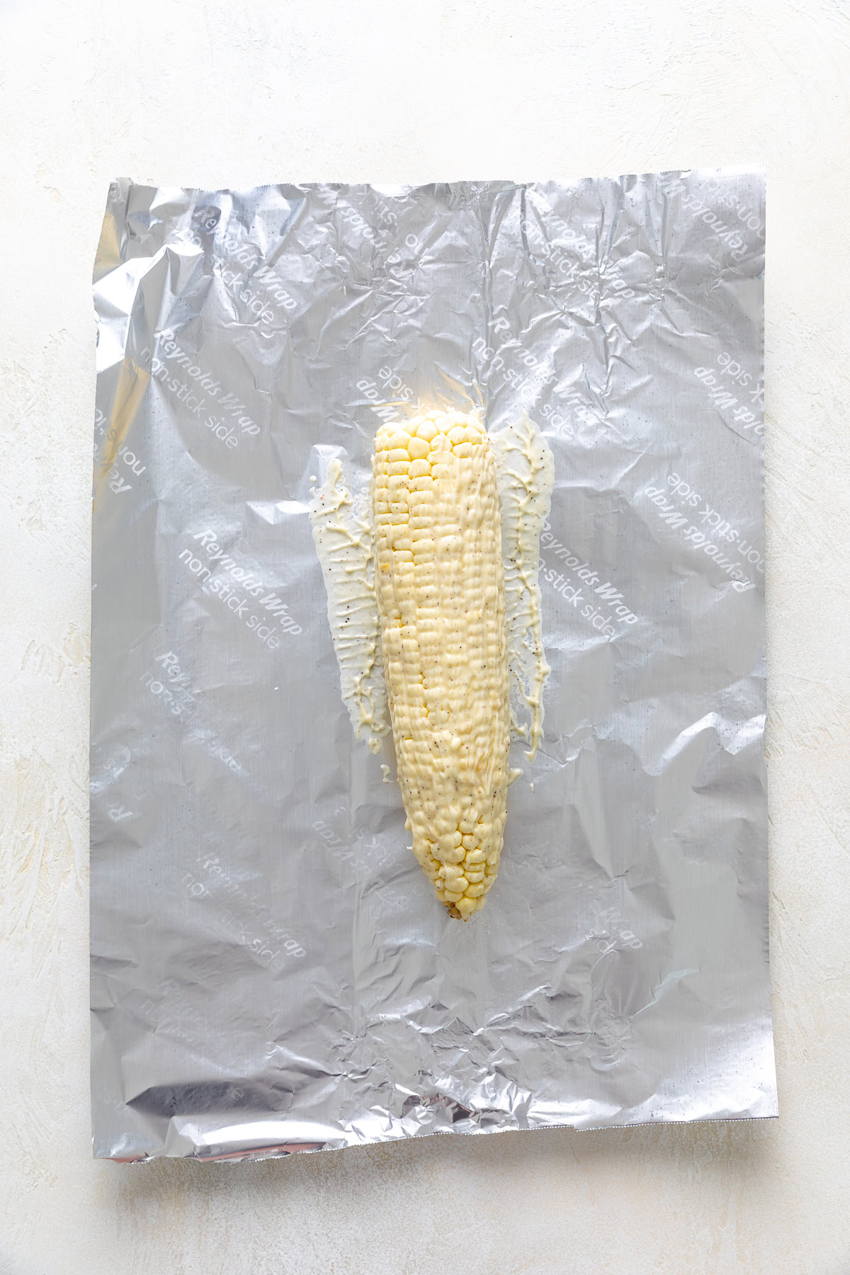 Corn on the cob coated with seasoned butter on aluminum foil.