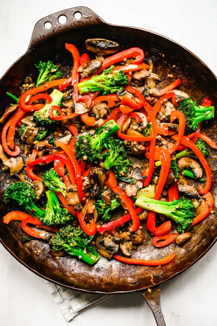 Close-up of broccoli, mushrooms, and red peppers cooking in a skillet.