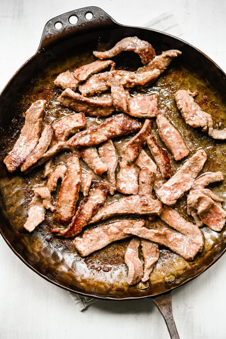 Close-up of browned steak strips cooking in a skillet.