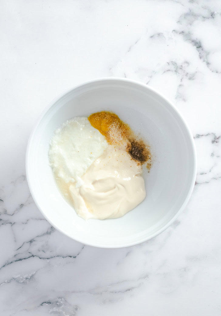 Mayonnaise, yogurt, Dijon mustard, lemon juice, salt, and pepper in a white mixing bowl.