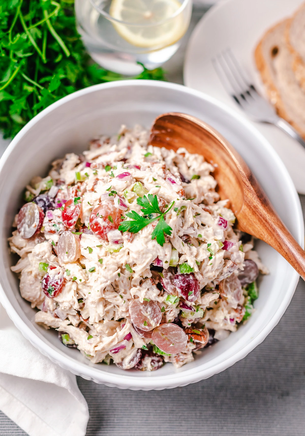 Wooden spoon holding chicken salad with grapes, pecans, celery, and parsley.