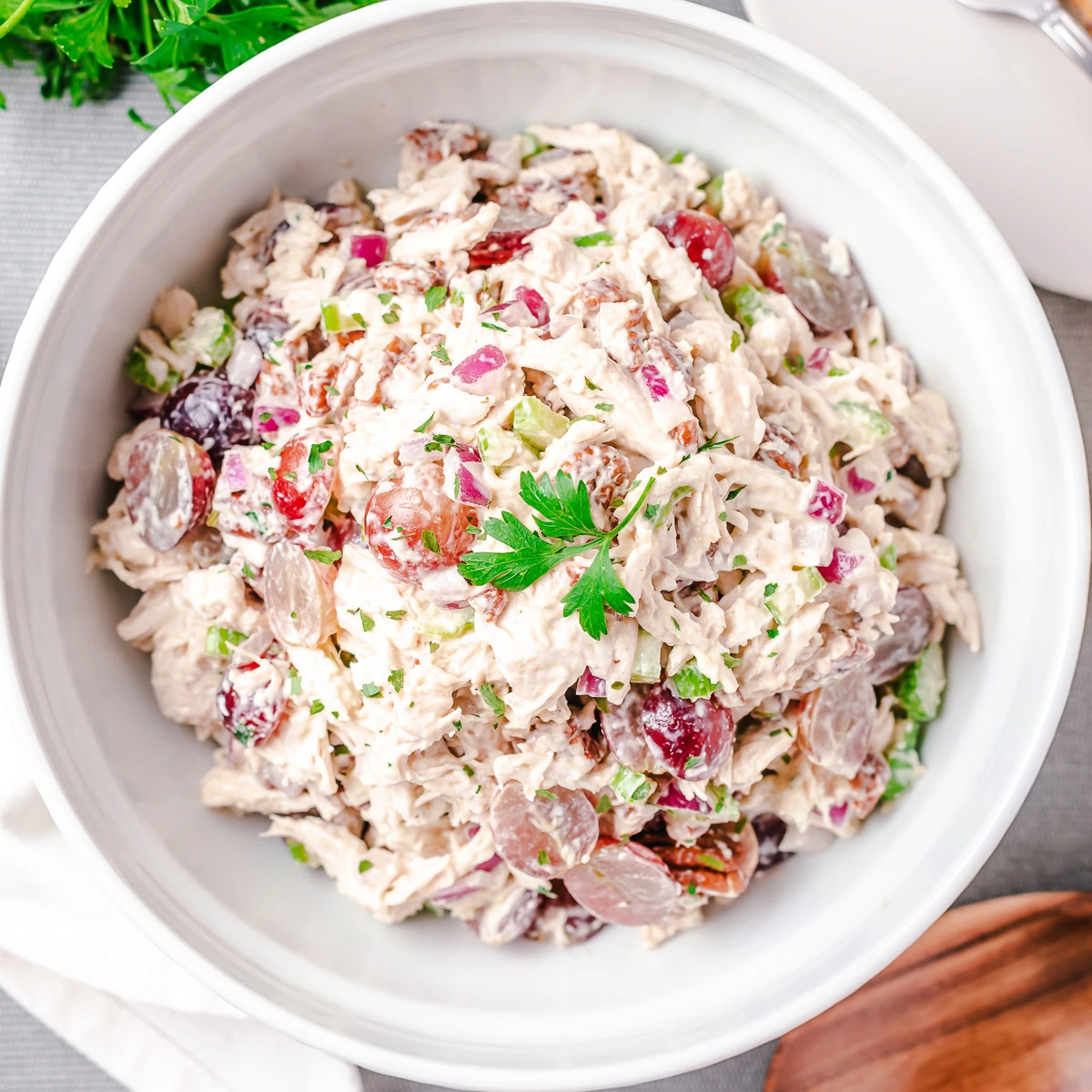 Creamy chicken salad with grapes, celery, pecans, red onion, and parsley in a white serving bowl.