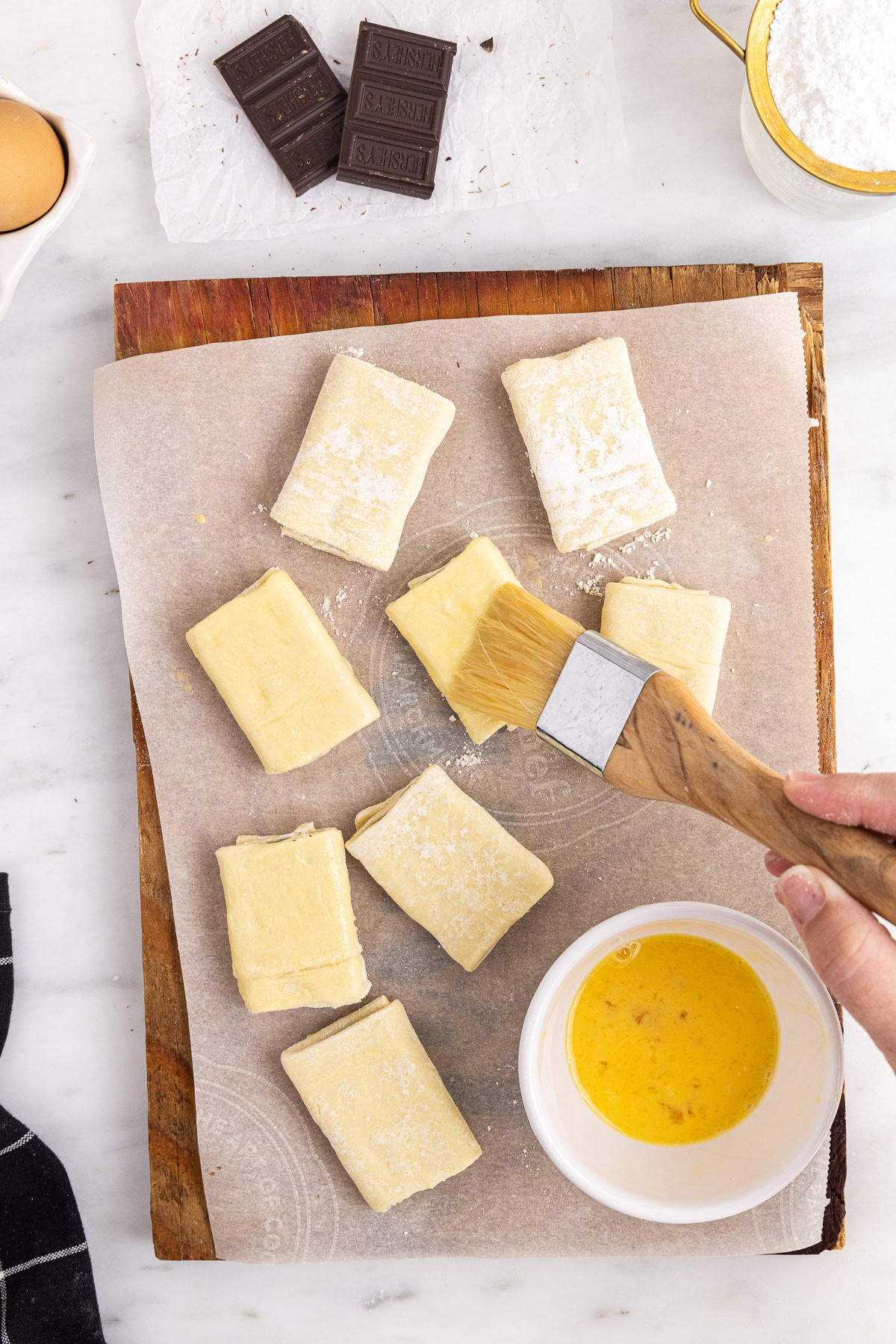 Chocolate-filled puff pastry rectangles brushed with egg wash on a parchment-lined baking sheet.