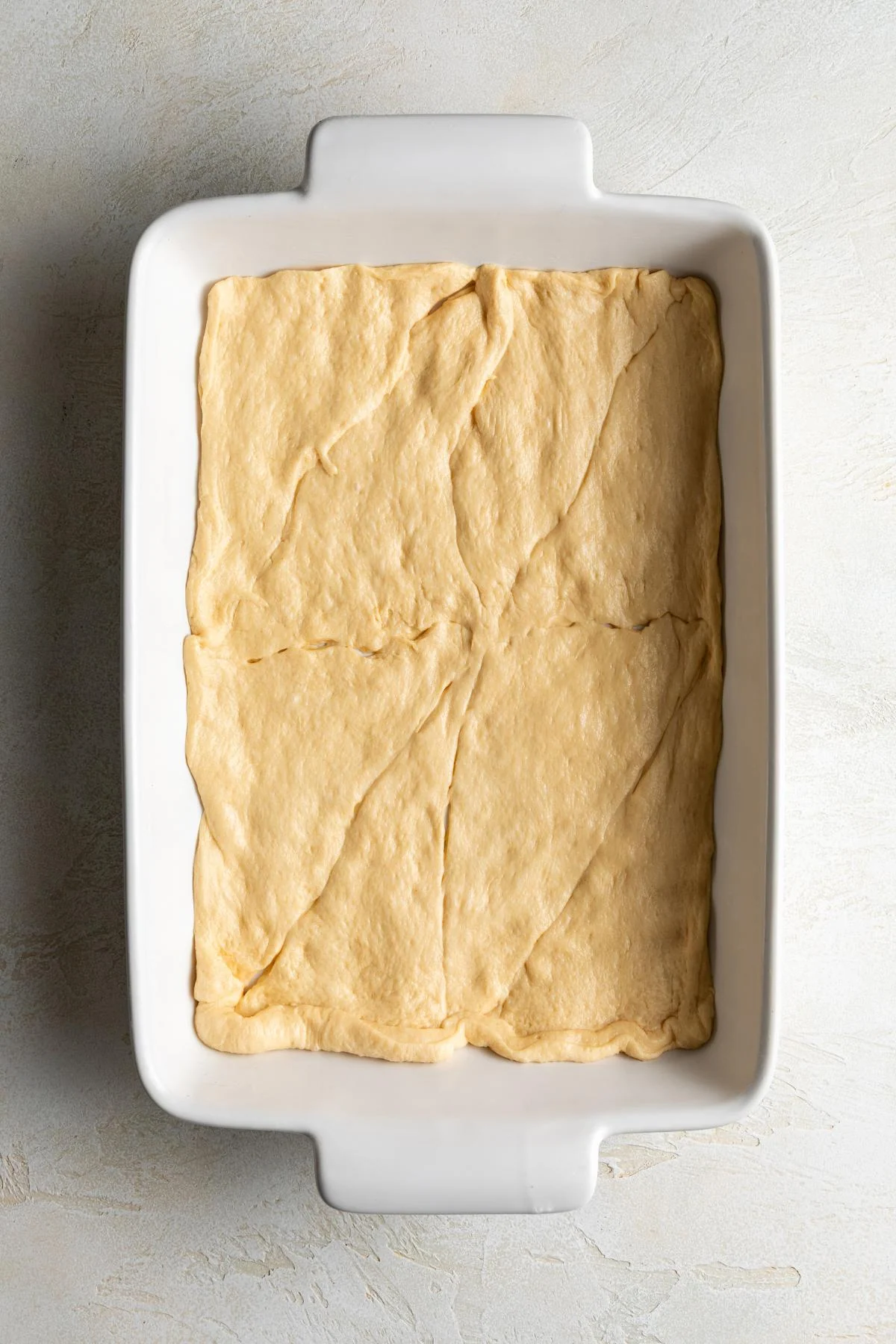 Crescent roll dough is pressed into a baking dish.