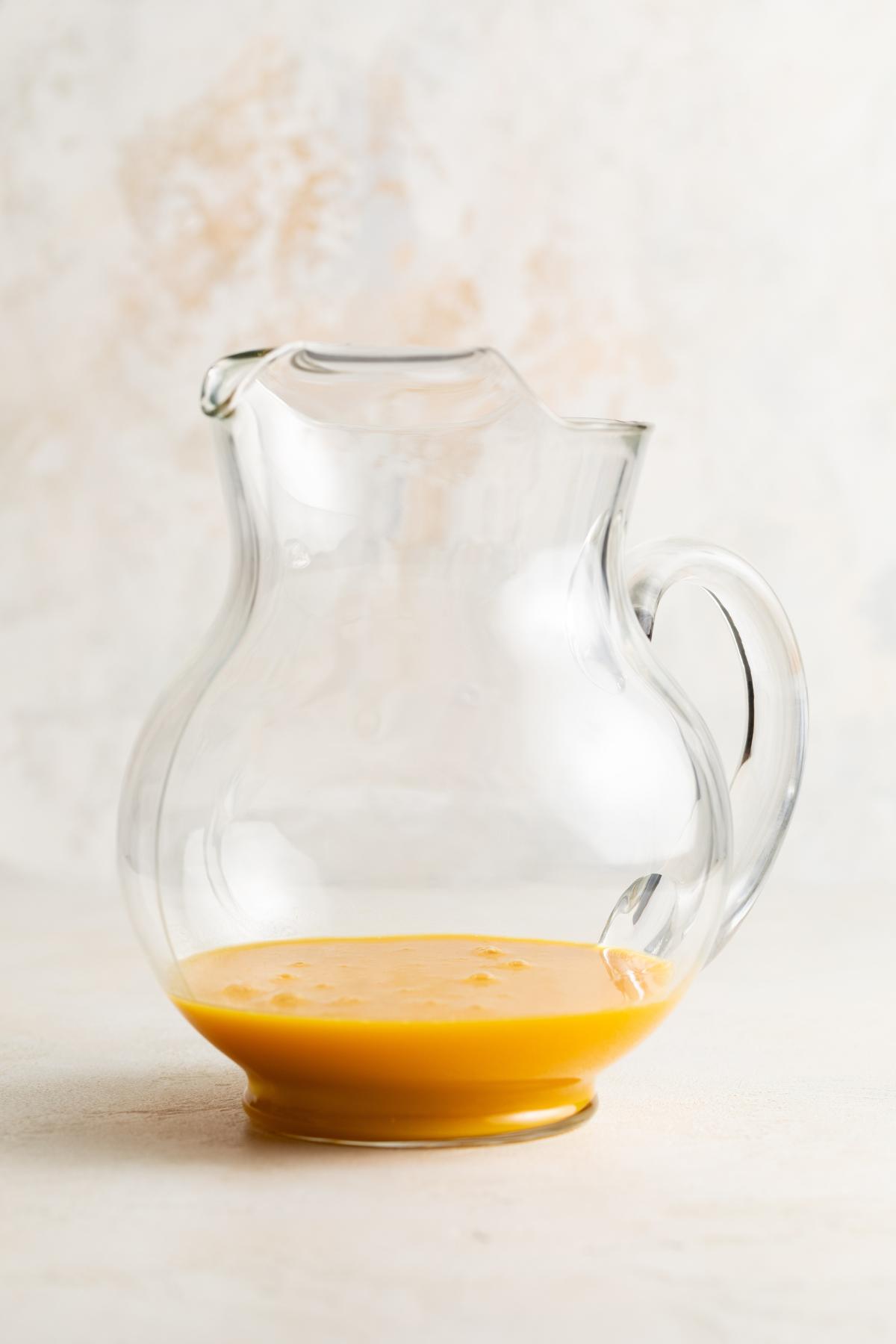 Thawed orange juice concentrate in the bottom of a clear glass pitcher.