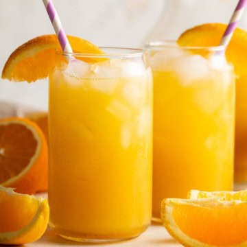 Close-up of two glasses of fizzy orange drink with ice and fresh orange slices.