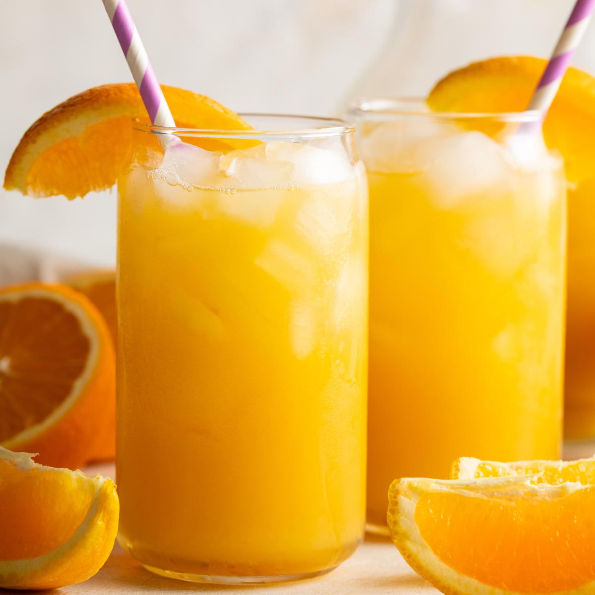 Close-up of two glasses of fizzy orange drink with ice and fresh orange slices.