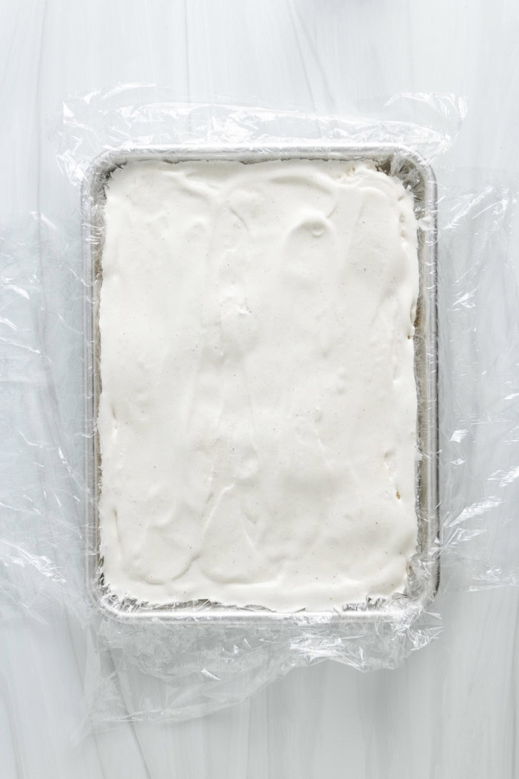 Vanilla ice cream spread into a plastic-lined baking pan.