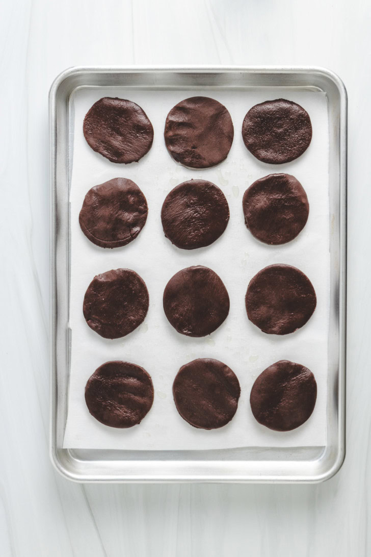 Chocolate cookie rounds on a parchment-lined baking sheet.