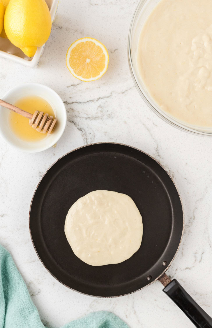 Lemon ricotta pancake batter cooking in a skillet.