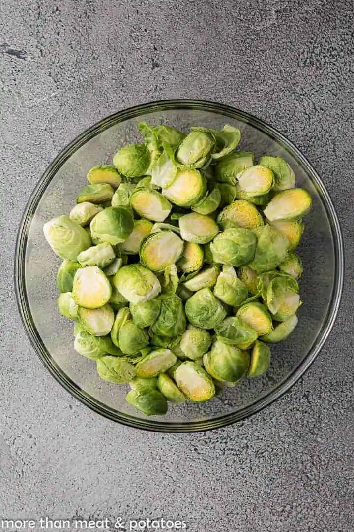 Halved Brussels sprouts in a glass mixing bowl.