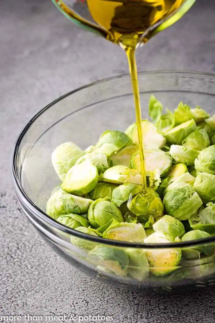 Olive oil being poured over Brussels sprouts.