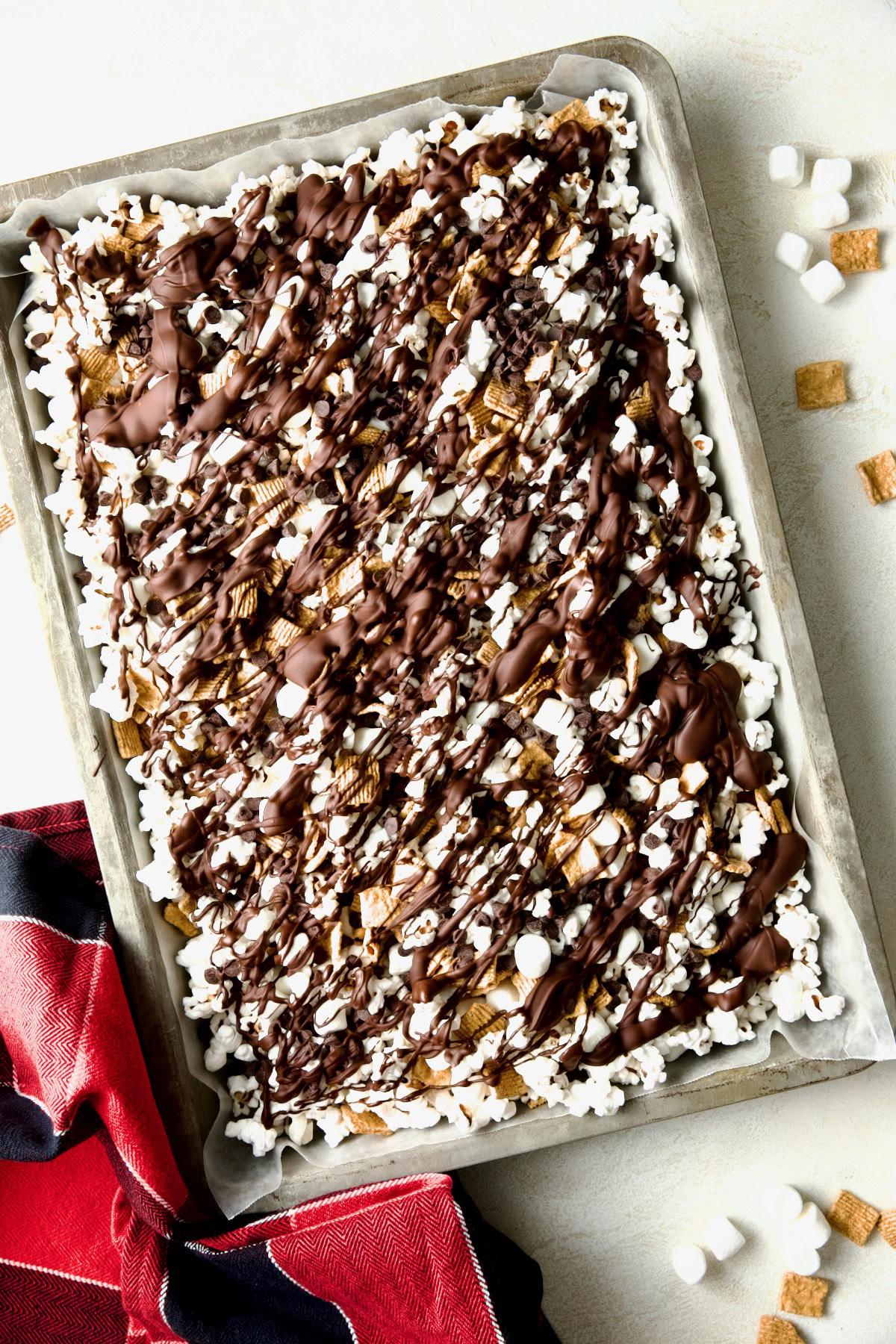 S'mores popcorn mix with cereal, marshmallows, and melted chocolate on a baking sheet.
