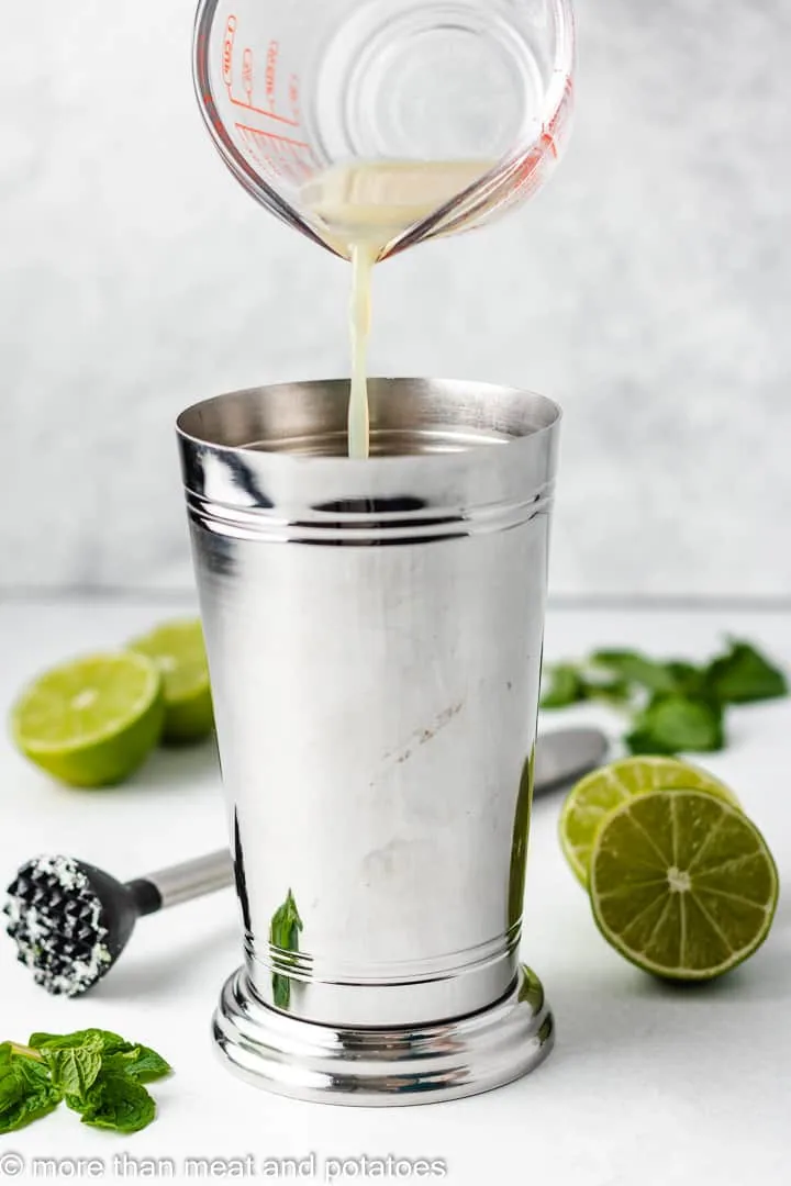 Lime juice being poured into a metal cocktail shaker.