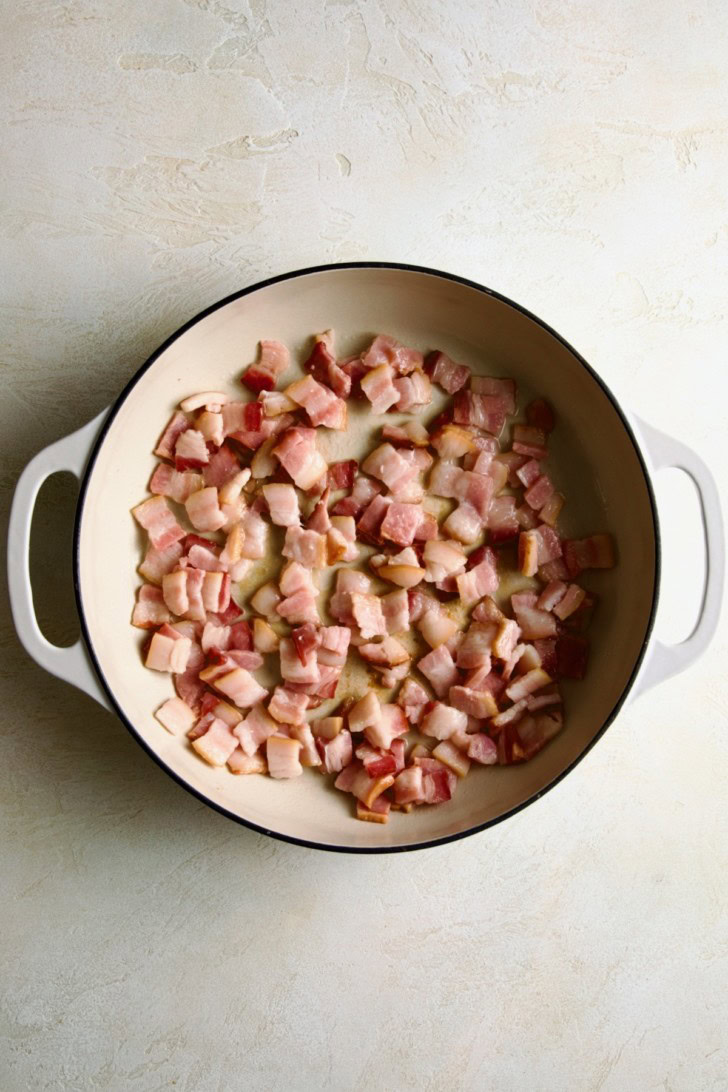 Diced bacon cooking in a white pot.