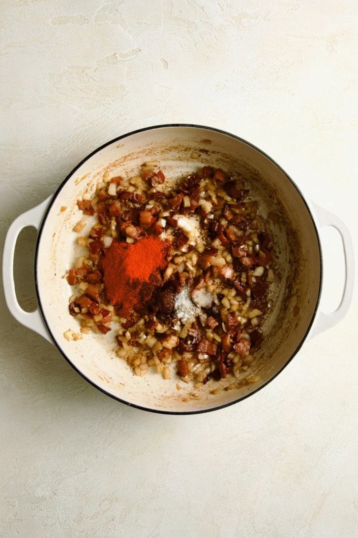 Bacon and onions with paprika and seasonings in a white pot.