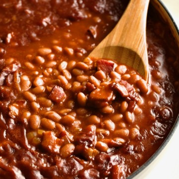 Close-up of baked beans with bacon and a wooden spoon.