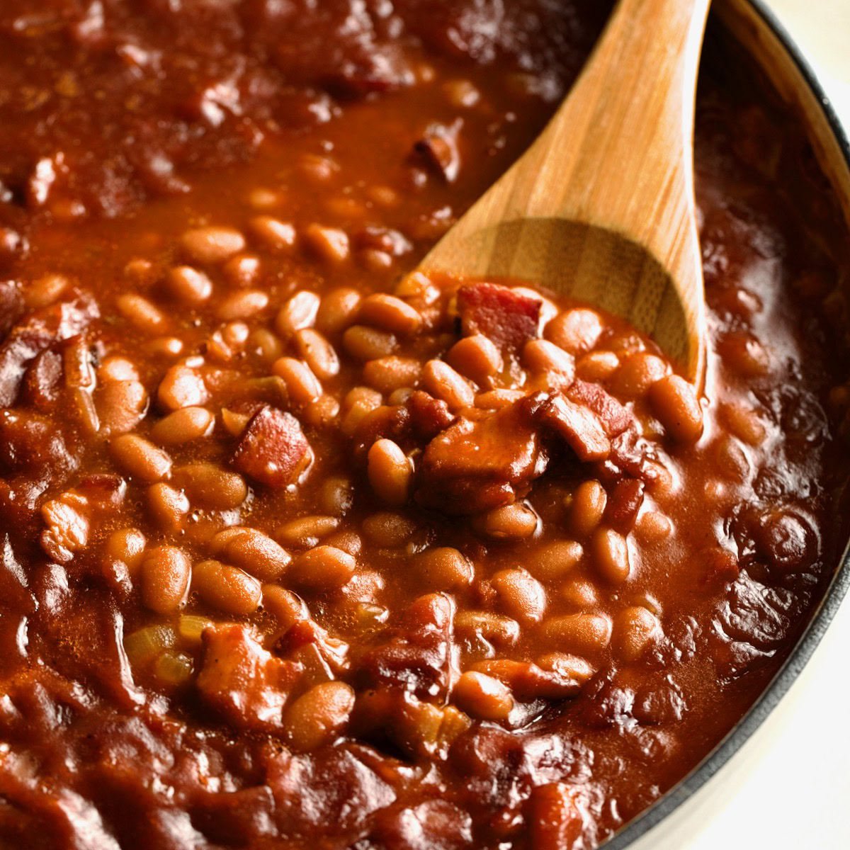 Close-up of baked beans with bacon and a wooden spoon.