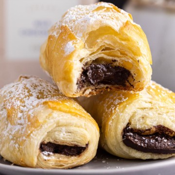 Chocolate-filled puff pastries dusted with powdered sugar, with one pastry cut open.