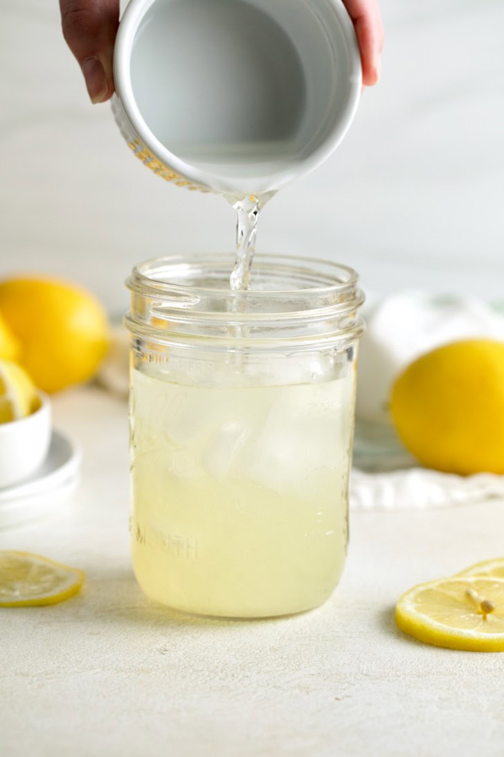 Lemon juice being poured into a mason jar with ice and vodka.