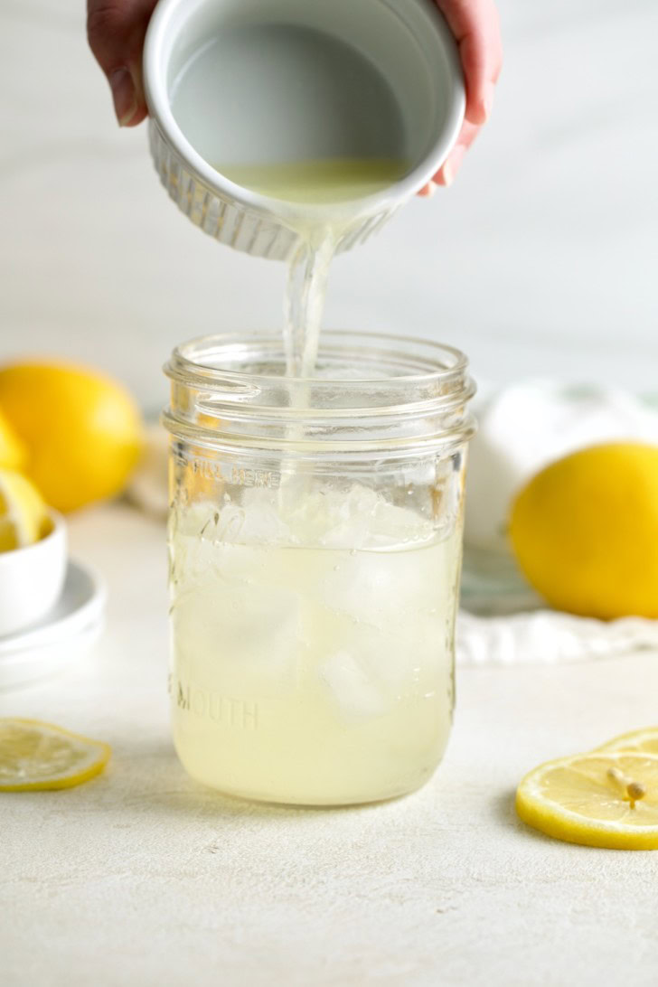 Simple syrup being added to a mason jar with lemon juice and ice.