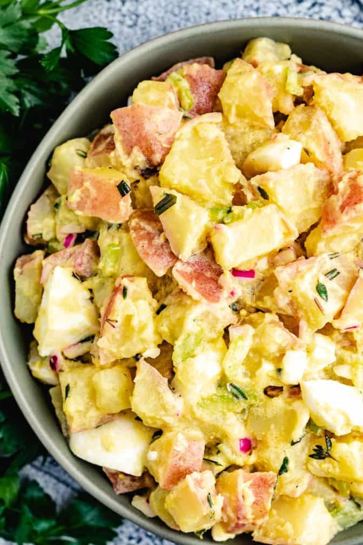 Close-up of potato salad with red potatoes, eggs, celery, and herbs.