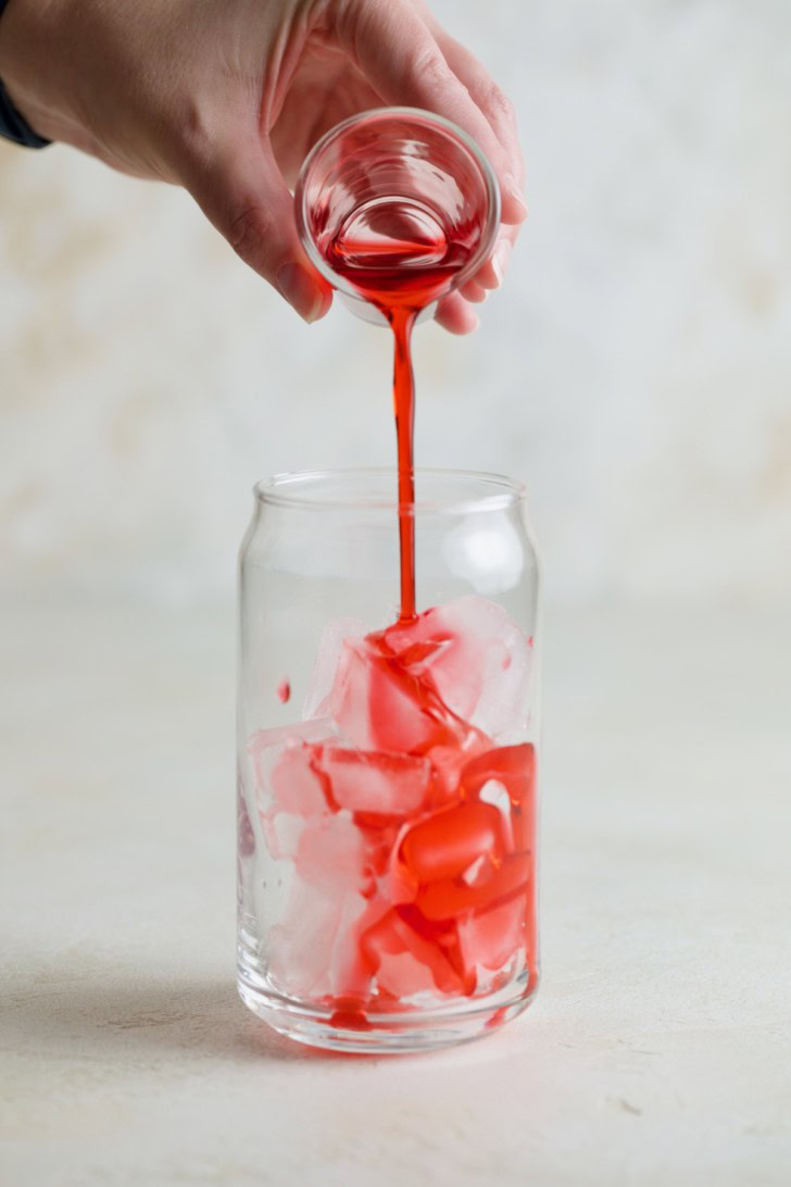 Raspberry syrup being poured over ice in a glass.