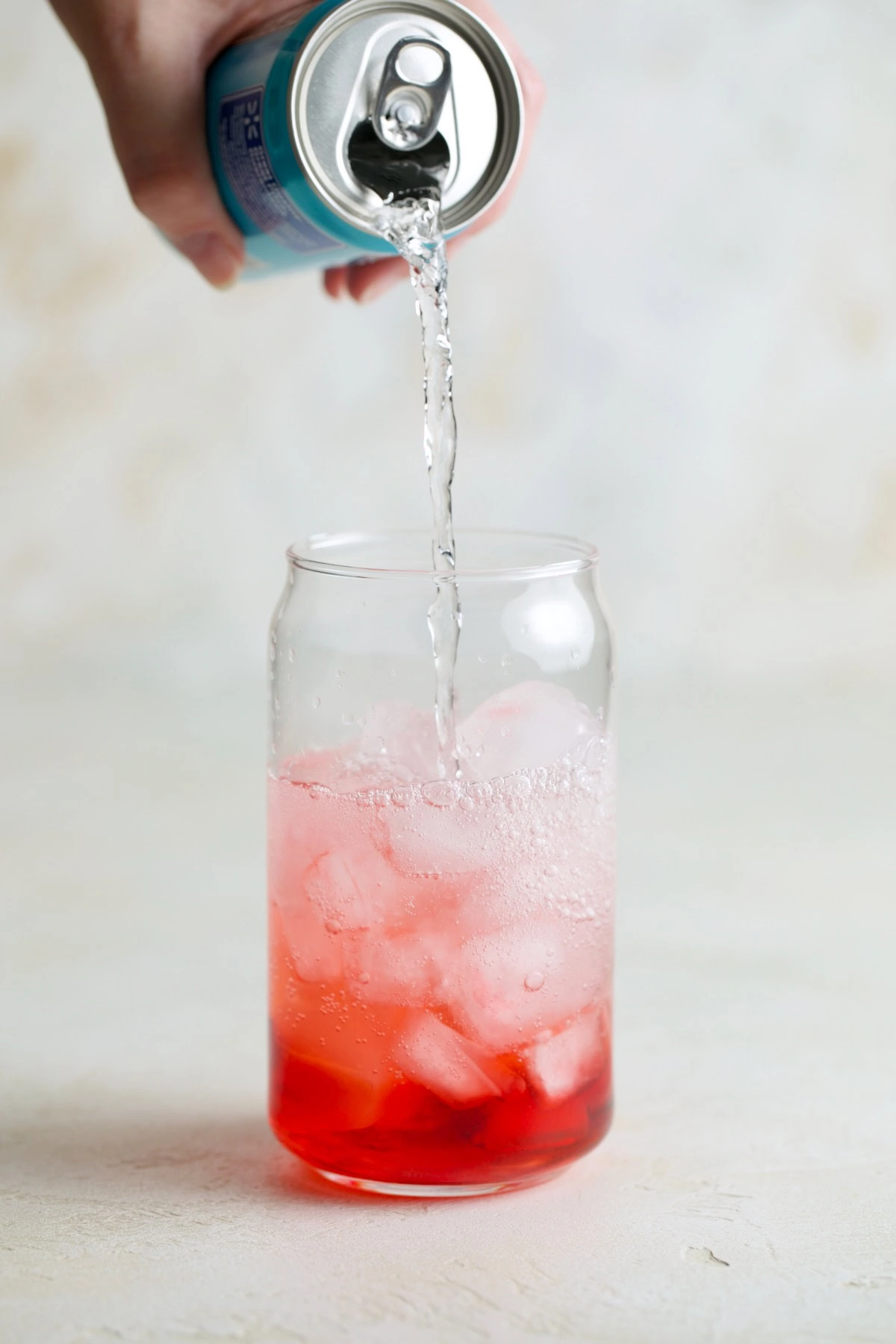 Club soda being poured over raspberry syrup and ice.