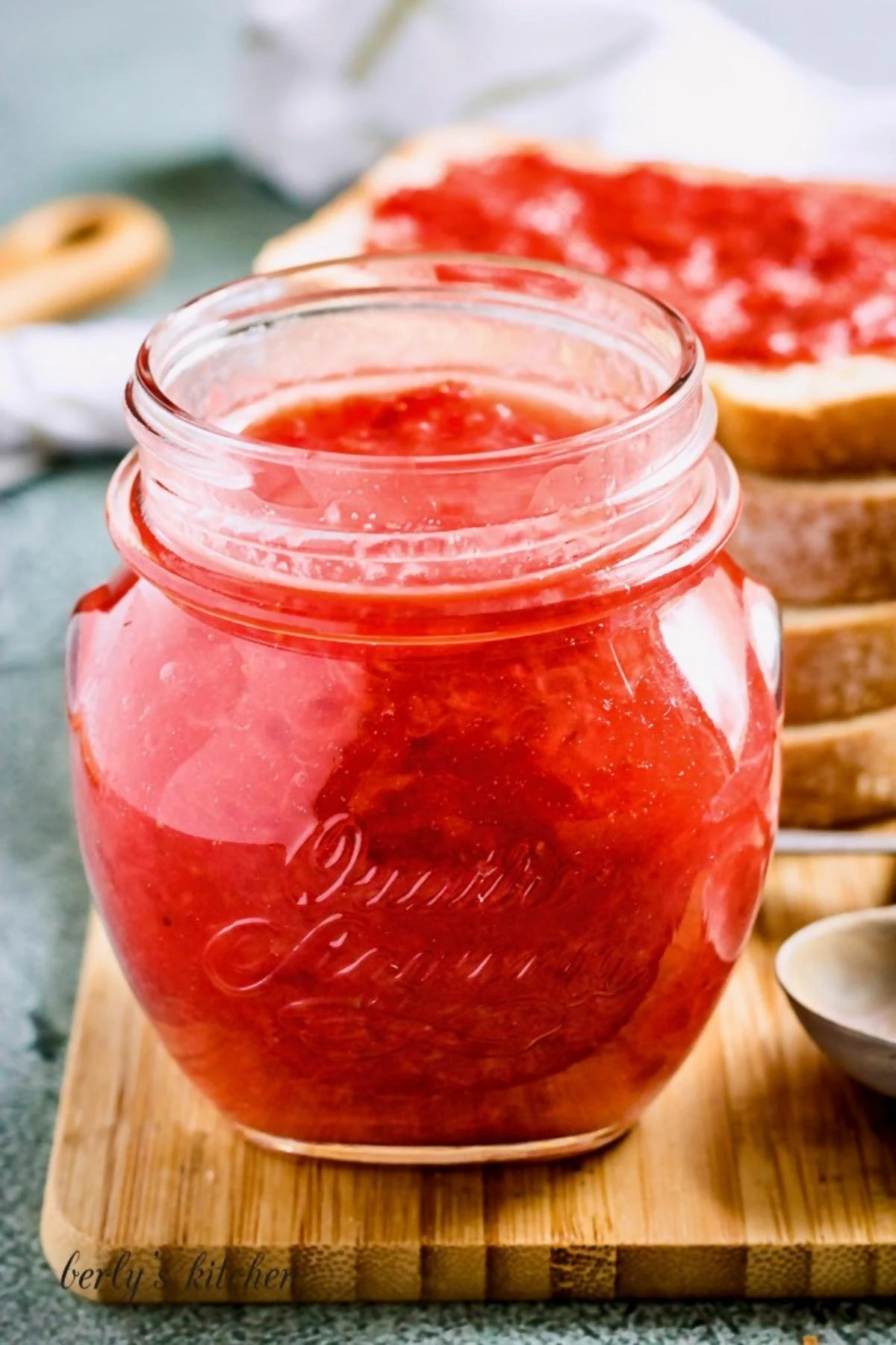 Strawberry jam in a jar with sliced bread.