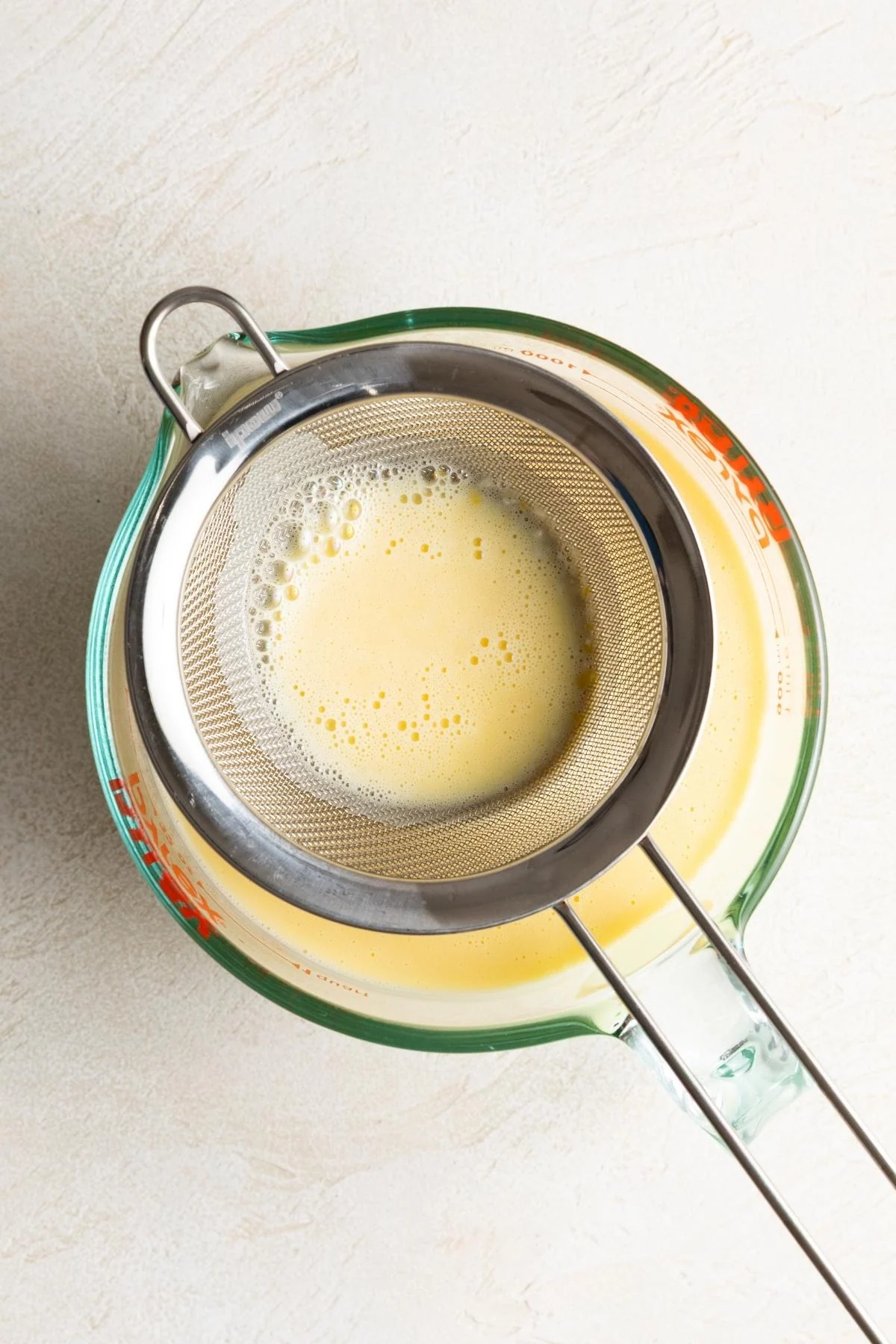Vanilla custard mixture being strained into a measuring cup.