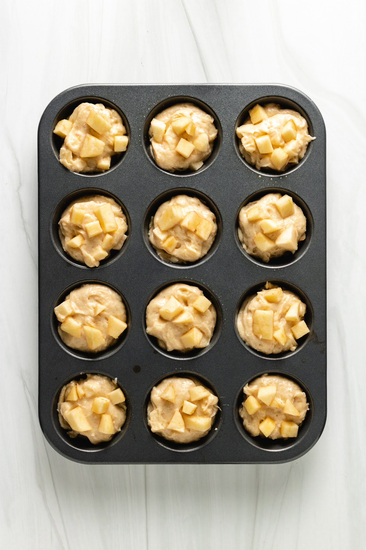 Diced apples dotted onto unbaked muffin batter in a muffin pan.