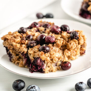 Slice of blueberry baked oatmeal next to fresh blueberries.
