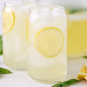 Glass of basil lemonade next to lemon wedge and basil leaves.