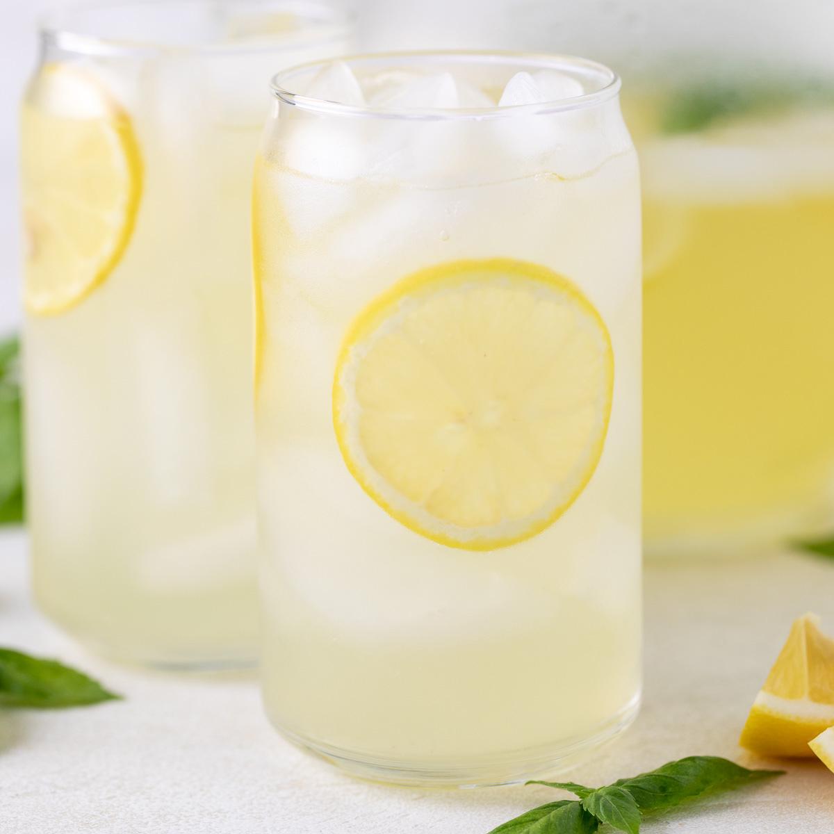 Glass of basil lemonade next to lemon wedge and basil leaves.