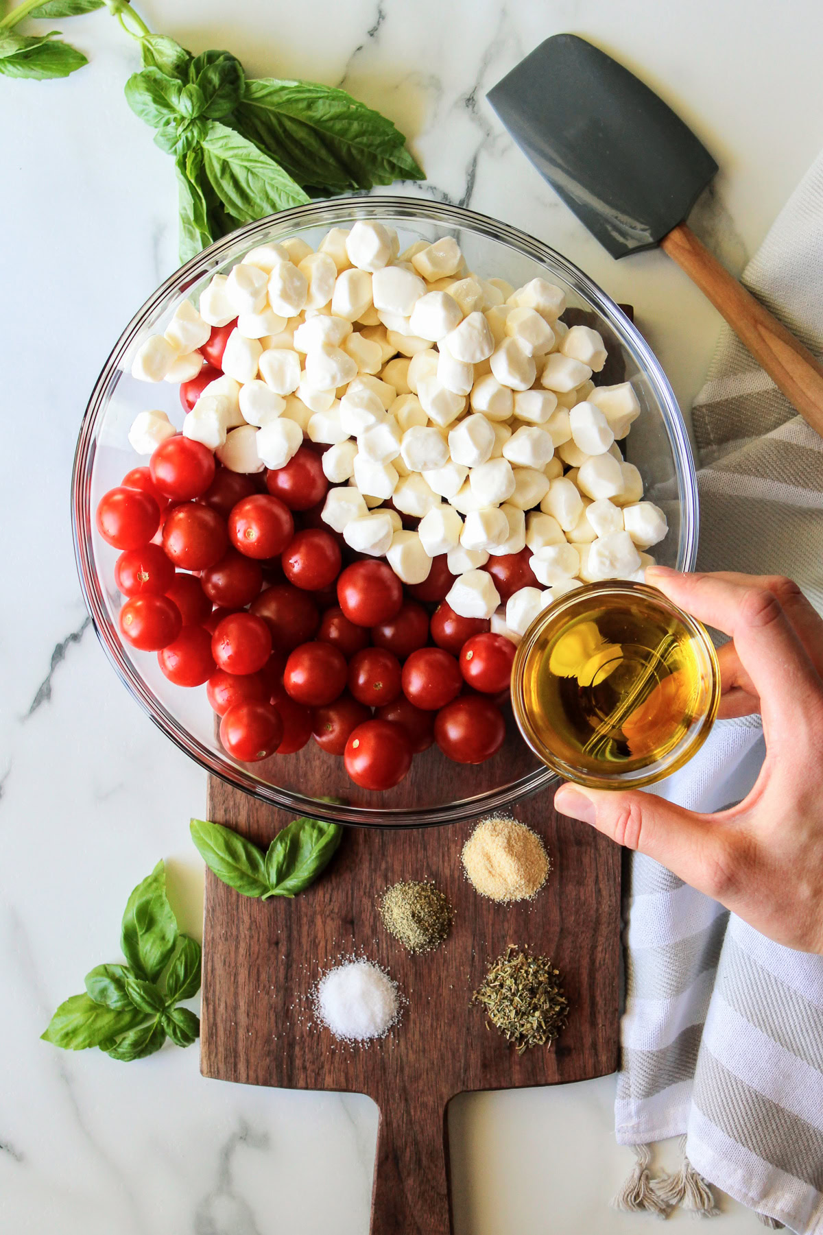 Olive oil being added to a bowl of cherry tomatoes and mozzarella.