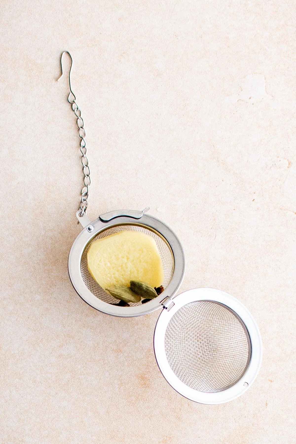 Tea infuser with ginger slice and cardamom for brewing tea.