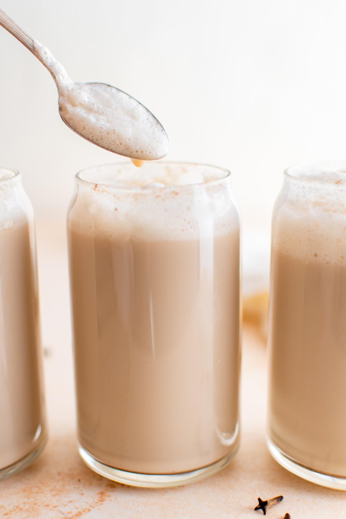 Chai latte in a glass with a spoonful of foam added.