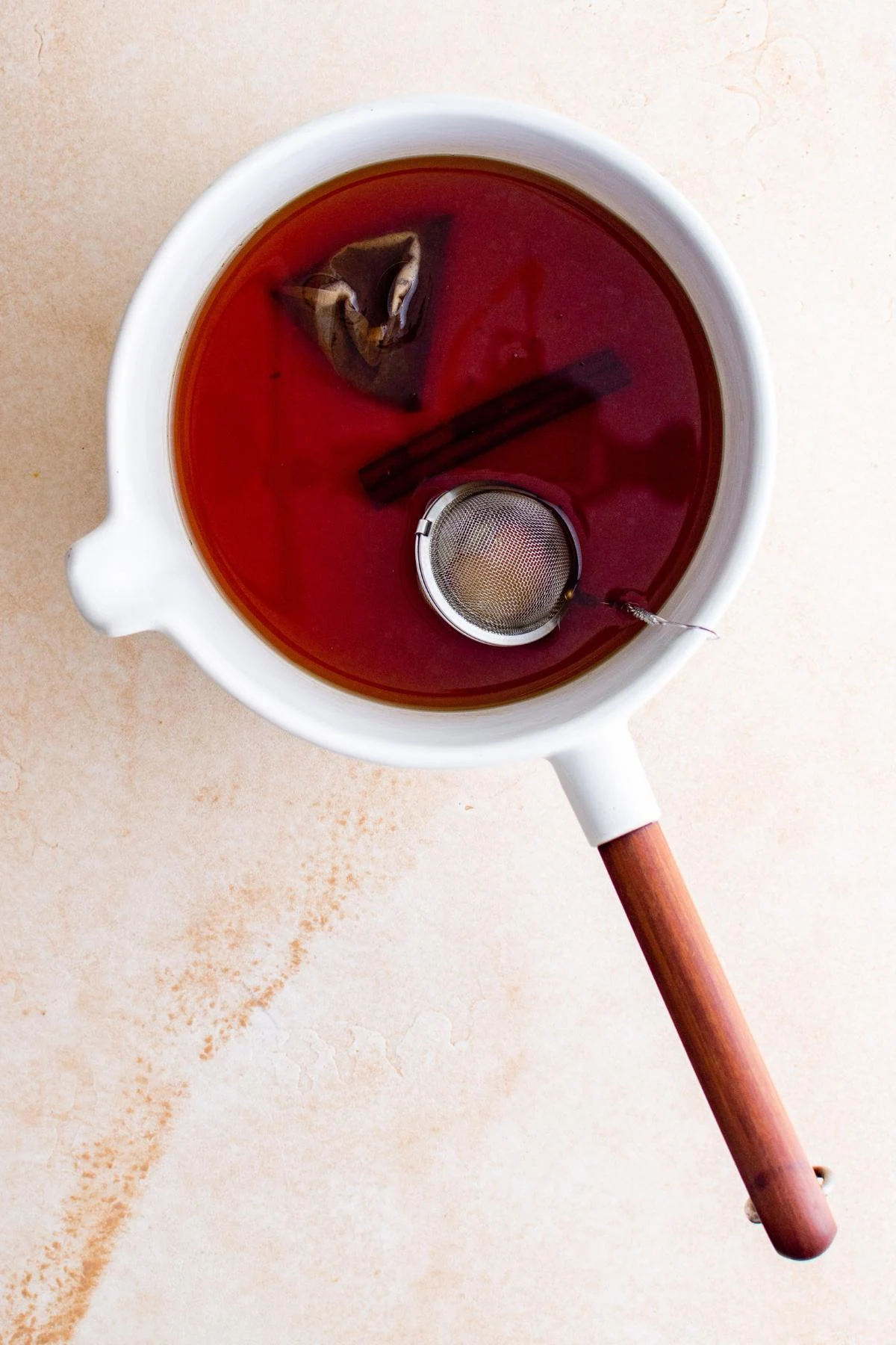 Herbal tea with tea bag and cinnamon stick in a white pan on light background.
