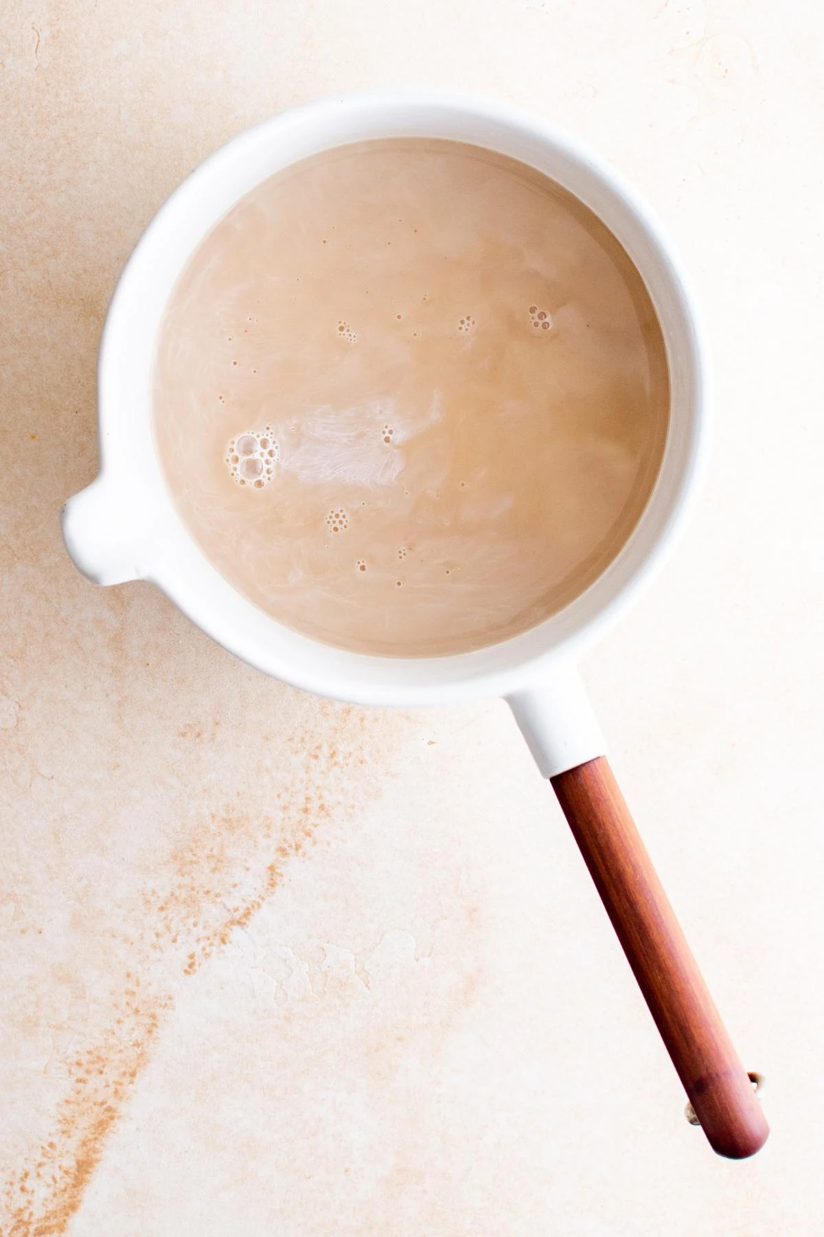 Creamy chai latte in a white mug with a wooden handle on a light surface.