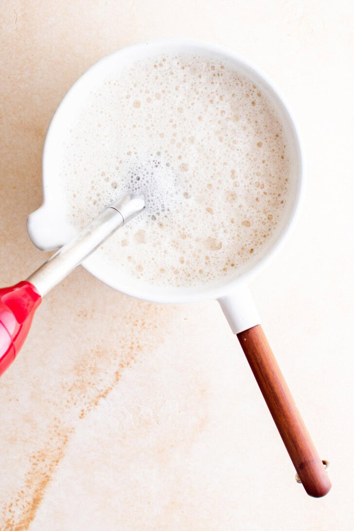 Milk froth in a white pan with a red and wooden handle.