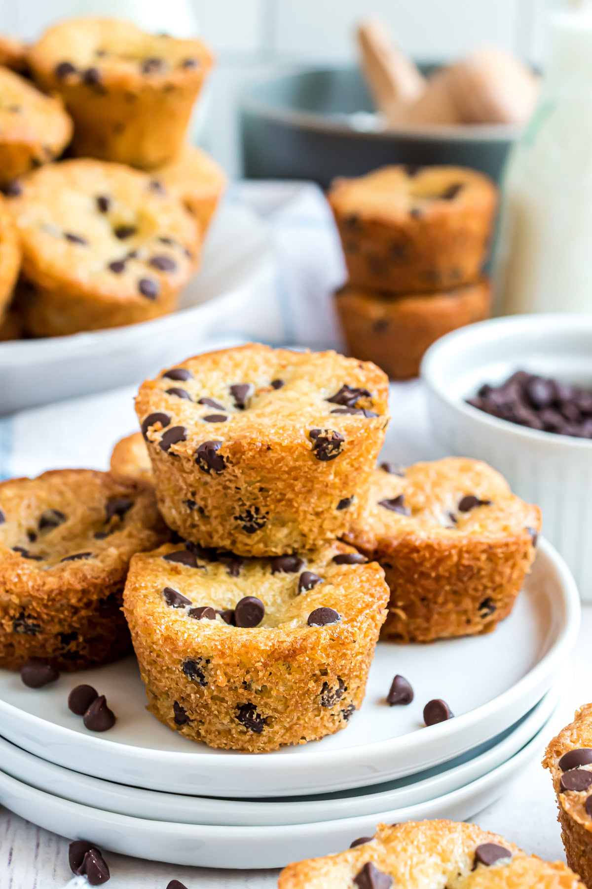 Mini chocolate chip muffins on a stack of white plates.