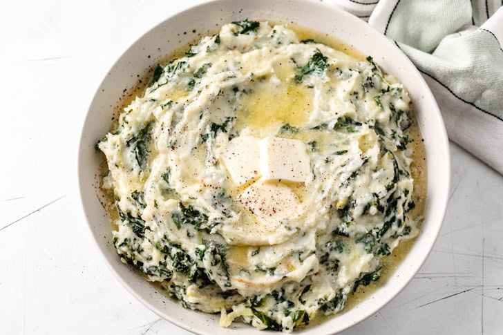 Bowl filled with kale, leeks, and mashed potatoes covered with melted butter.