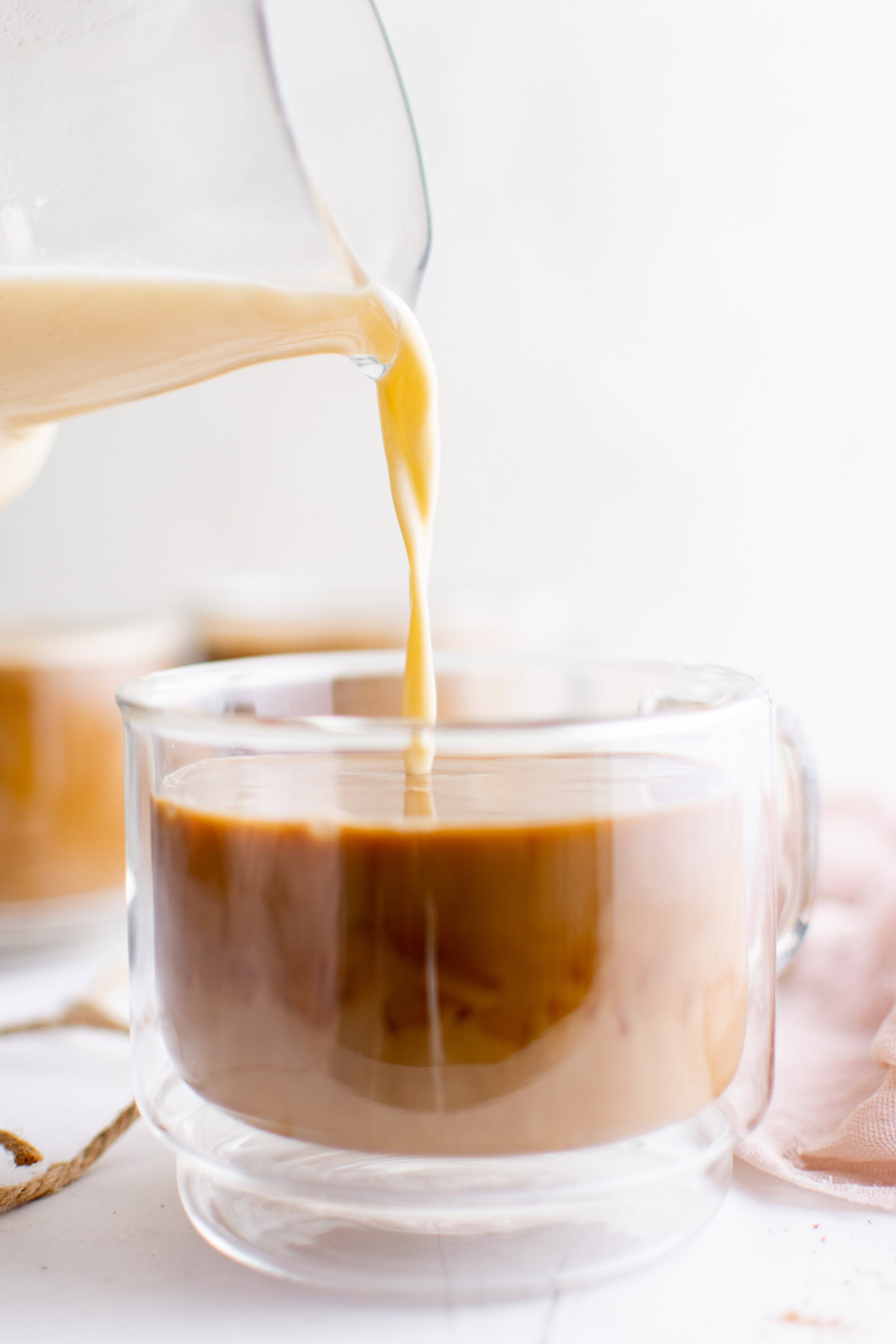 Eggnog latte being poured into a glass mug.