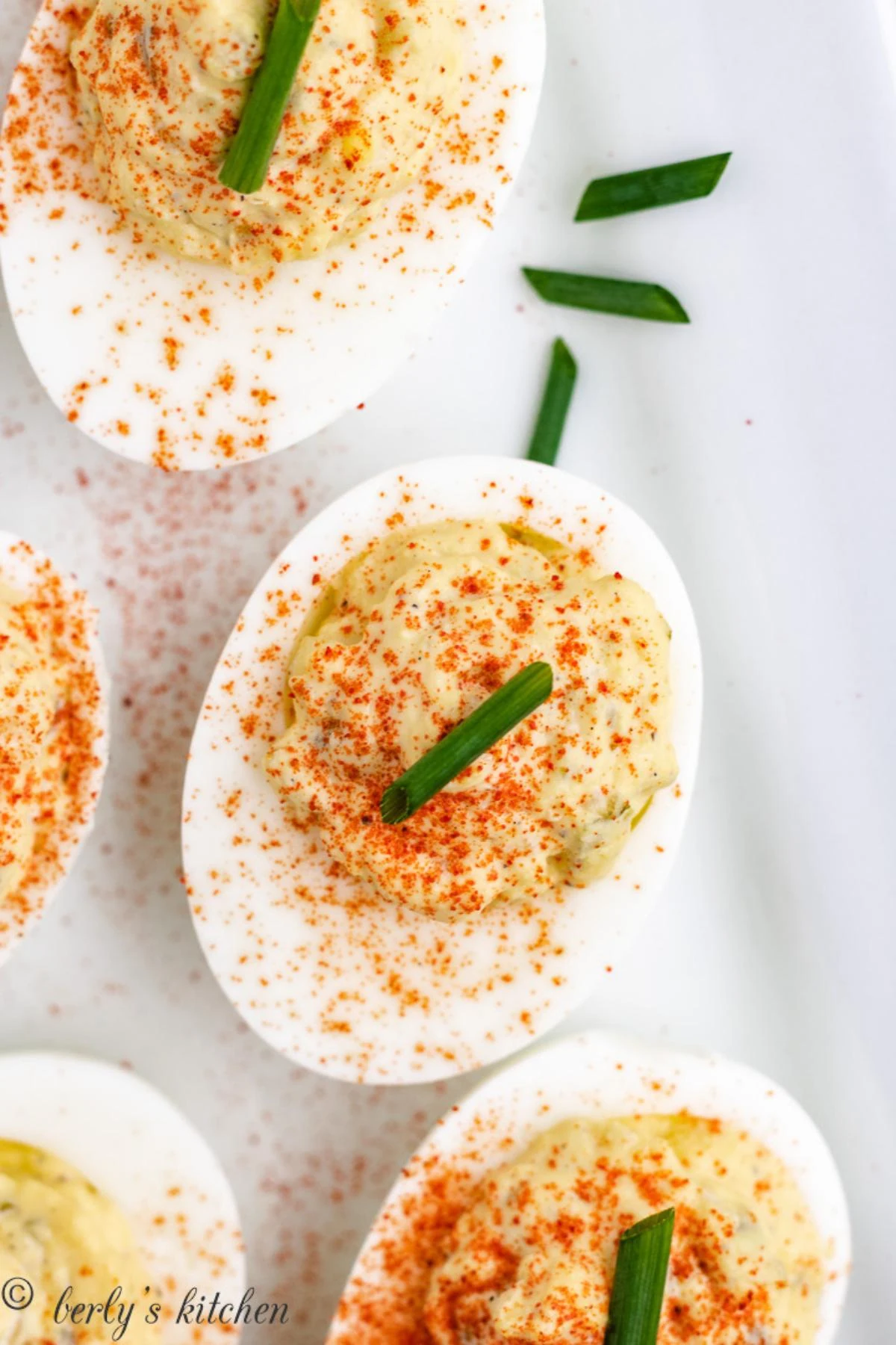 Deviled eggs garnished with paprika and green onion on a white plate.