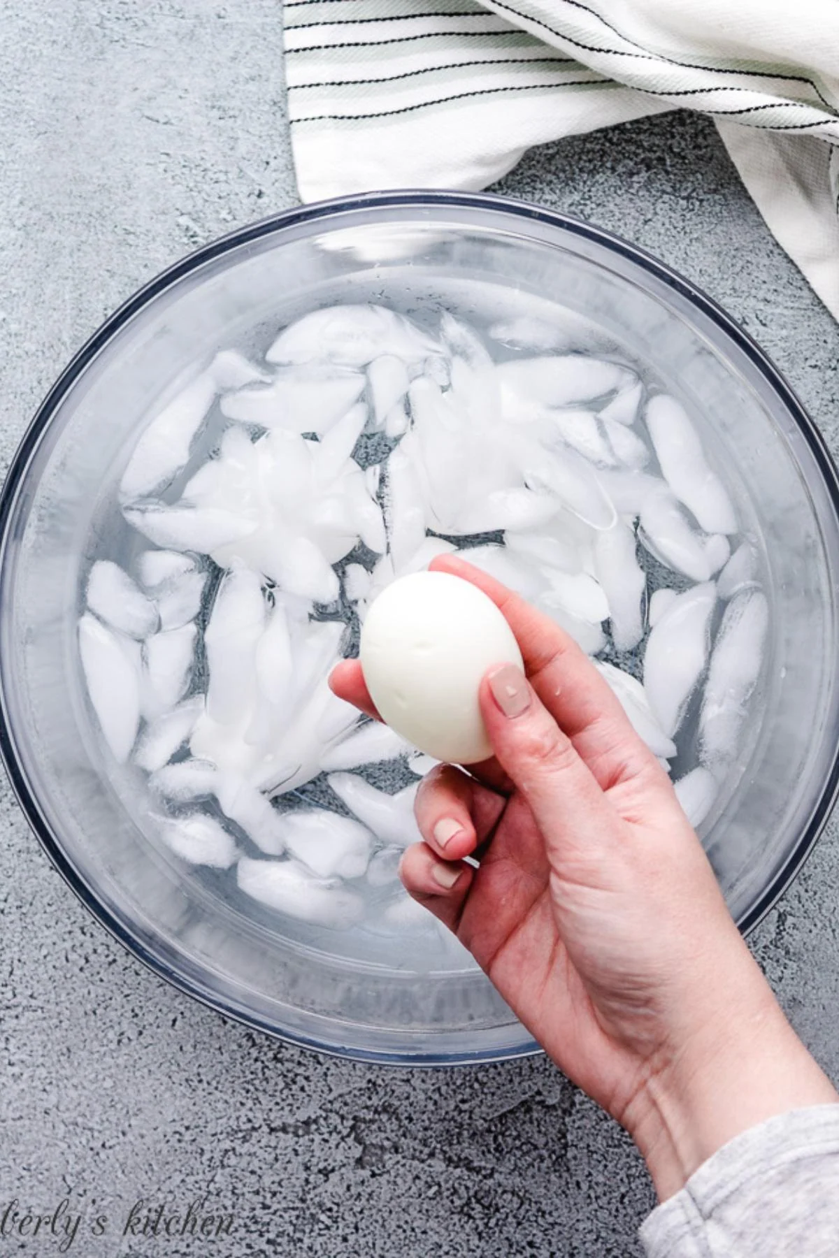 Hand holding a boiled egg over a bowl of ice cubes and water.