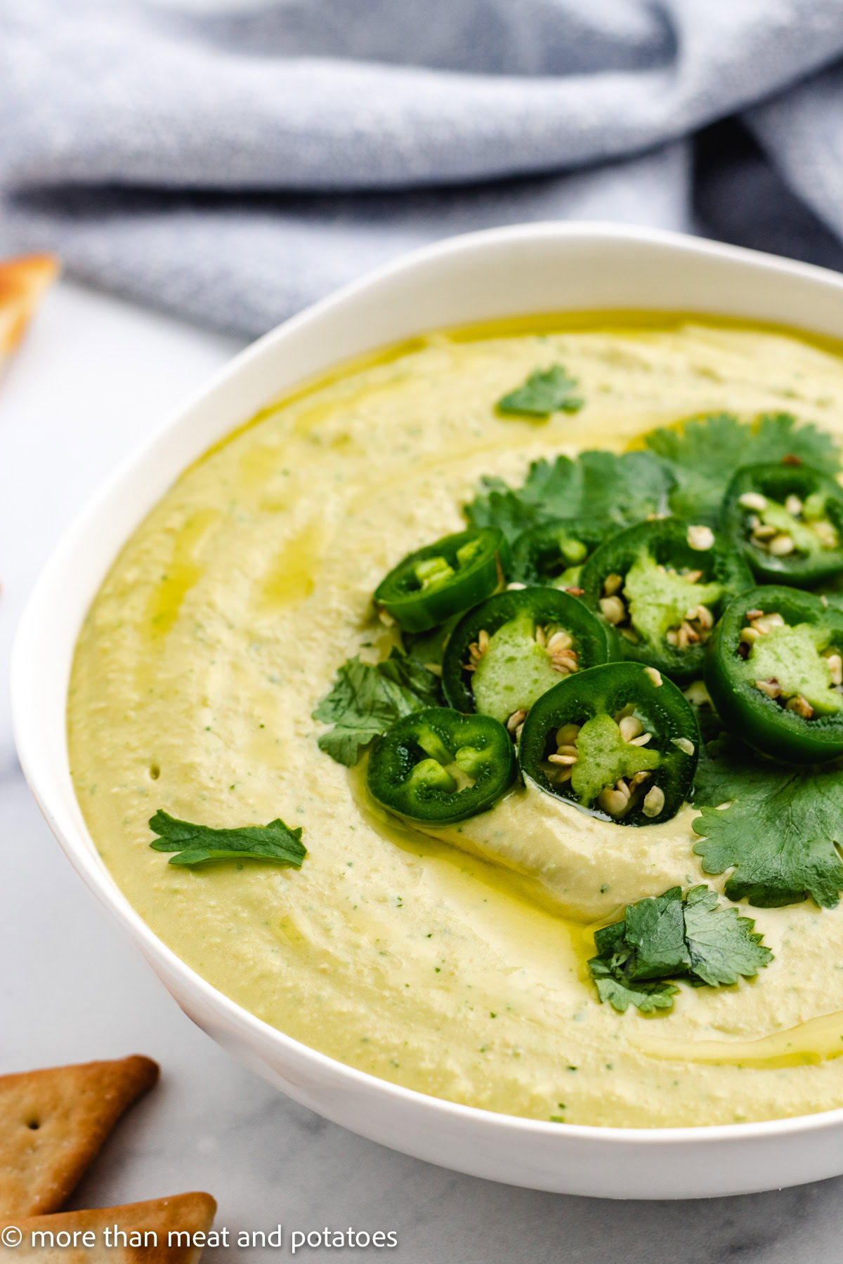 Close up view of creamy jalape&ntilde;o cilantro hummus in a white bowl.