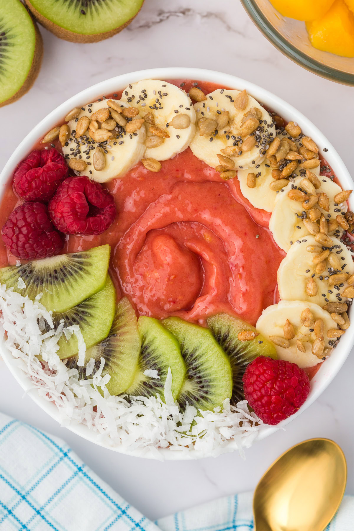 Overhead view of a mango raspberry smoothie bowl with fruit toppings.