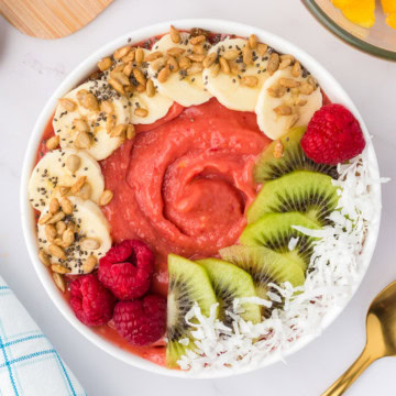 Close up view of a mango raspberry smoothie bowl next to a gold spoon.