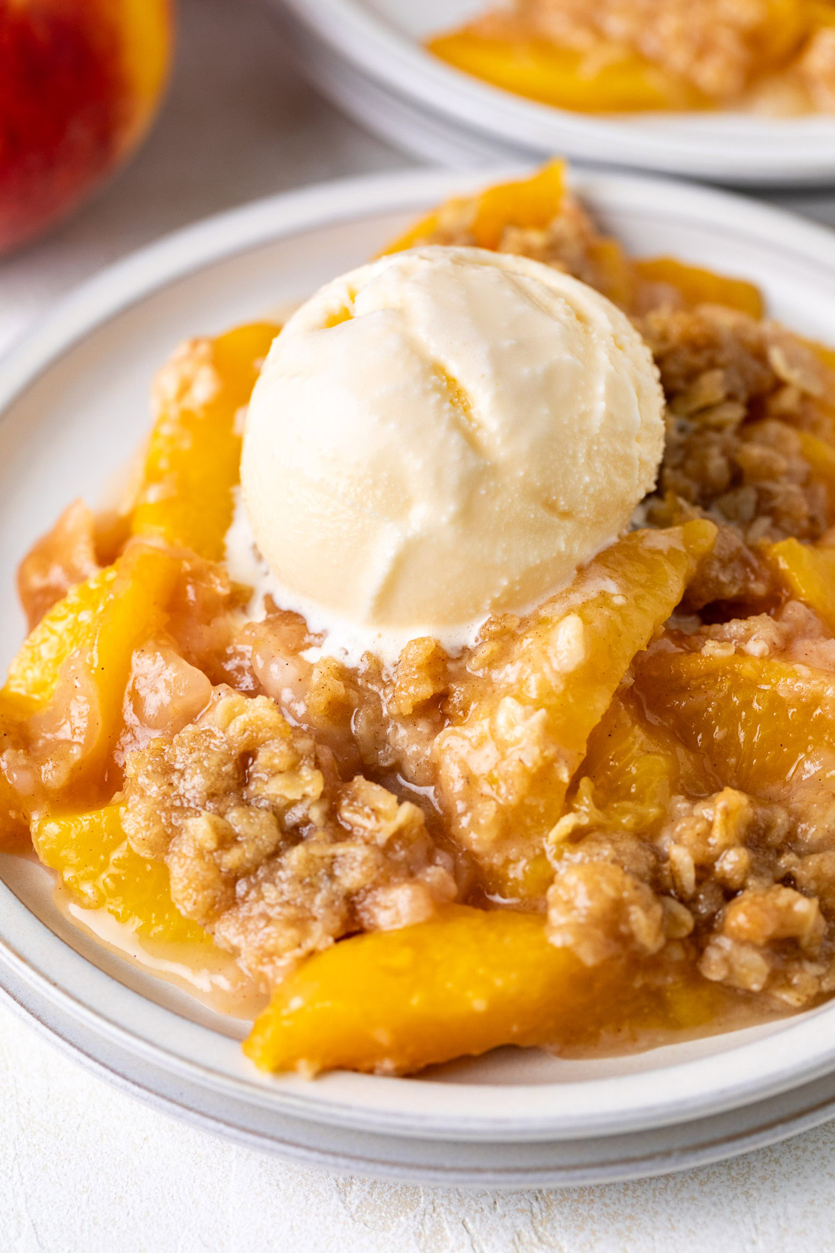 Close-up of peach crisp topped with vanilla ice cream.